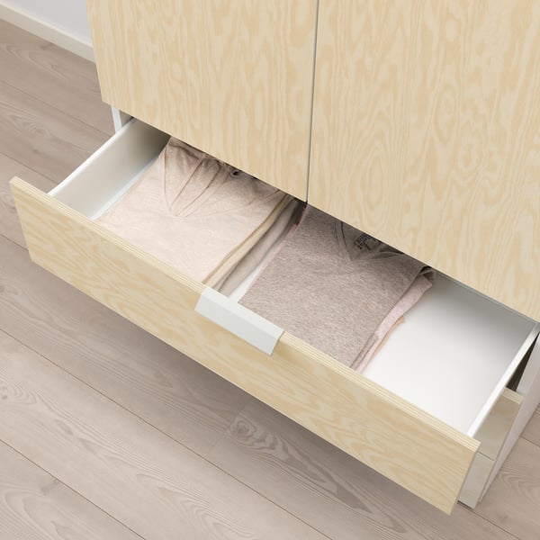 Cassetto in legno aperto, che rivela i vestiti ben piegati all'interno. Parte di un sistema di archiviazione con cornici di colore chiaro.