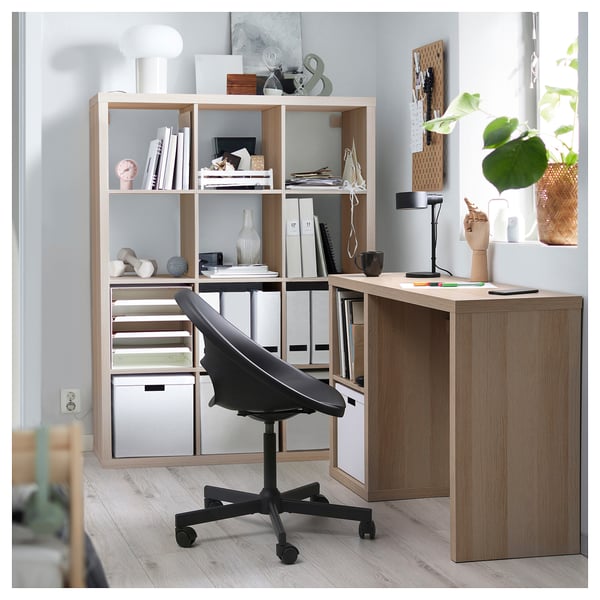 Home office moderno con scaffalature KALLAX marrone chiaro e scrivania lidkullen, sedia da ufficio nera, vari oggetti esposti sugli scaffali.