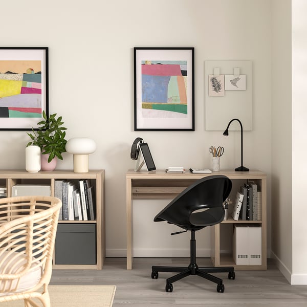 Ufficio domestico con scrivania in legno, sedia girevole nera e librerie, adornate con opere d'arte colorate e decorazioni ordinate.