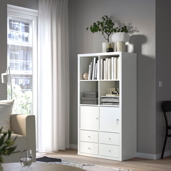 Uno scaffale KALLAX bianco in una stanza luminosa con uno scaffale aperto che espone libri e oggetti decorativi e un armadietto con serratura per una conservazione sicura.