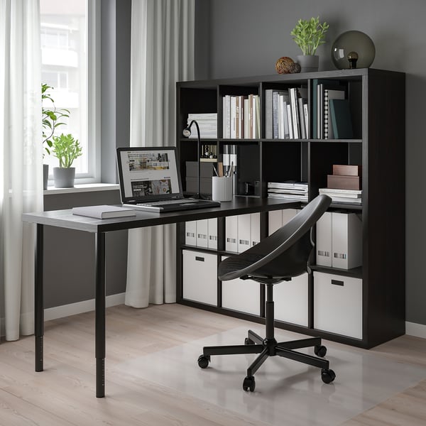 Home office moderno con scaffale e scrivania KALLAX neri. Sedia, laptop, libri e piante.
