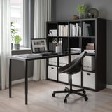 Home office moderno con scaffale e scrivania KALLAX neri. Sedia, laptop, libri e piante.