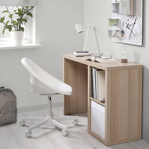 Configurazione minimalista dell'home office con scrivania KALLAX in legno chiaro, sedia bianca e arredamento moderno.