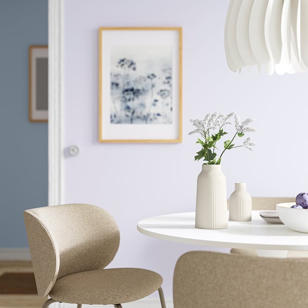 Vaso minimalista KAPKASTANJ con texture scanalata, che tiene fiori bianchi sul tavolo da pranzo con sedie.