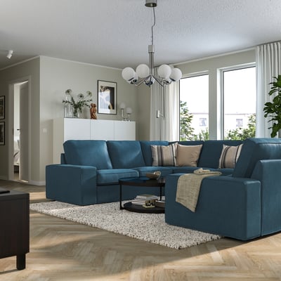 Soggiorno moderno: grande divano KIVIK blu con morbidi cuscini, elegante tavolino, pavimento in legno chiaro e ampie finestre.