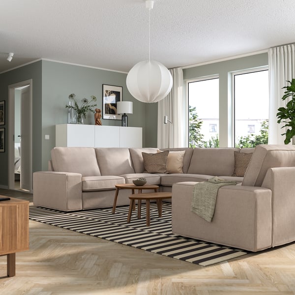 Soggiorno moderno con divano beige KIVIK, tappeto a righe, lampada a sospensione e tavolino della metà del secolo. Il divano è grande, può ospitare più posti.