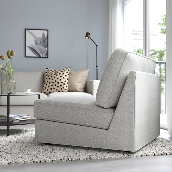 Soggiorno moderno con divano letto KIVIK con ampia finestra. Tappezzeria grigia, cuscini, tavolino con tulipani e lampada da terra.