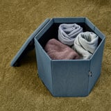Cestino esagonale che contiene coperte piegate su moquette beige.