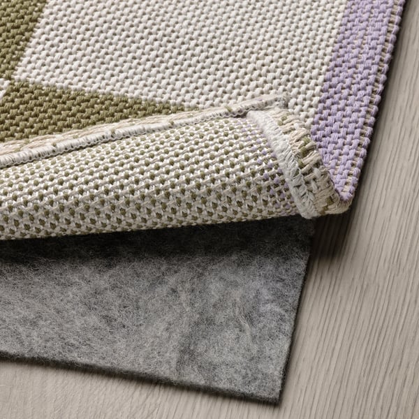 Tappeto colorato con motivo intrecciato e supporto in feltro poggia sul pavimento in legno.