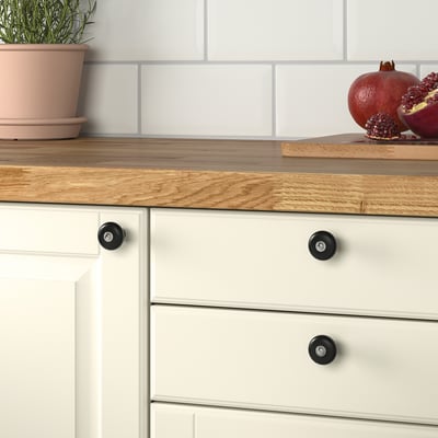 Piano di lavoro in legno con armadio bianco, pomelli neri opachi, melograno e pianta.