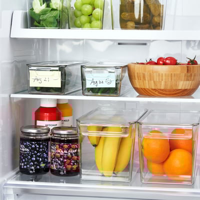 Frigorifero con frutta e barattoli organizzati, utilizzando contenitori impilabili trasparenti con coperchi ed etichette per freschezza e facile accesso.