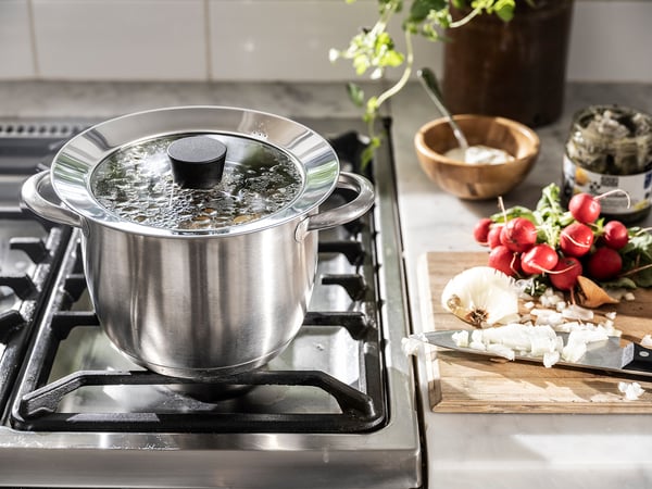 Coperchio in vetro, verdure, tagliere sul fornello.