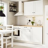 Cucina moderna con bancone in rovere, vasi sospesi e piante. Armadi bianchi, fornello, lavello e zona pranzo.