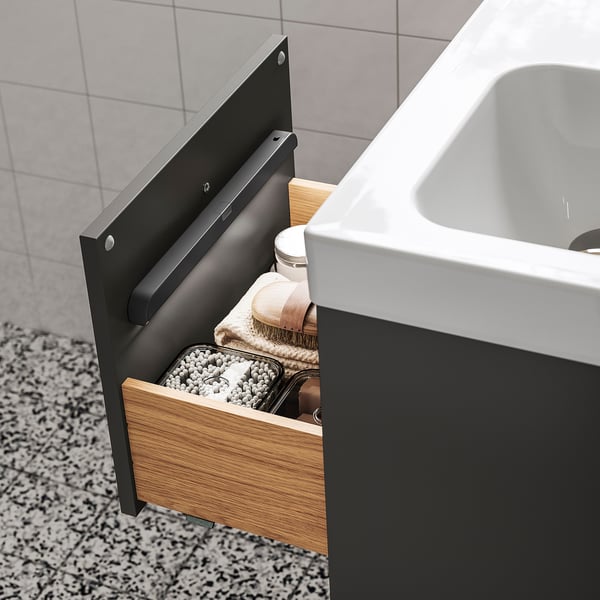 Il cassetto in legno aperto rivela un'illuminazione soffusa, organizzando vestiti e accessori in un ambiente bagno, mettendo in mostra la comodità e lo stoccaggio moderni.