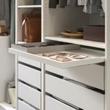 Organizer per armadio KOMPLEMENT bianco con vassoio estraibile per portafogli e accessori, circondato da vestiti e una borsa appesa.