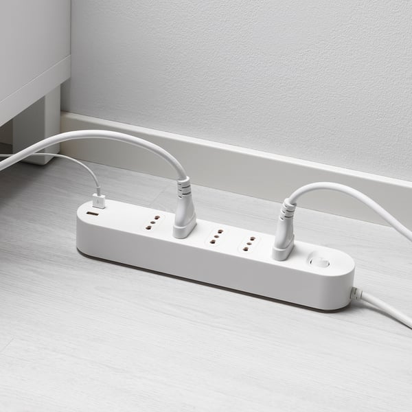 Multipresa bianca con porte usb su pavimento in legno, collegata a una presa a muro.