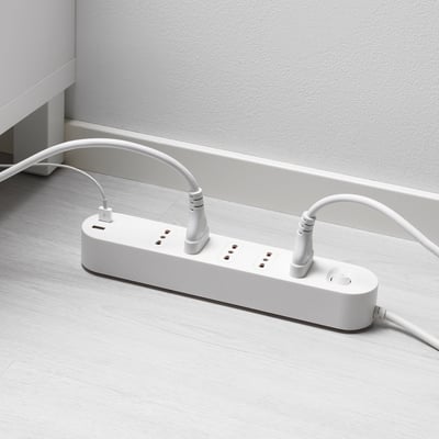 Multipresa bianca con porte usb su pavimento in legno, collegata a una presa a muro.
