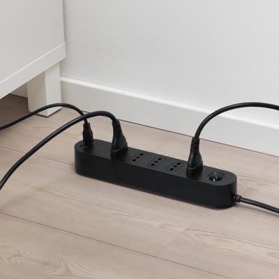 Adattatore multi-presa nero su pavimento in legno con 5 prese e 2 porte USB, ricarica più dispositivi contemporaneamente.