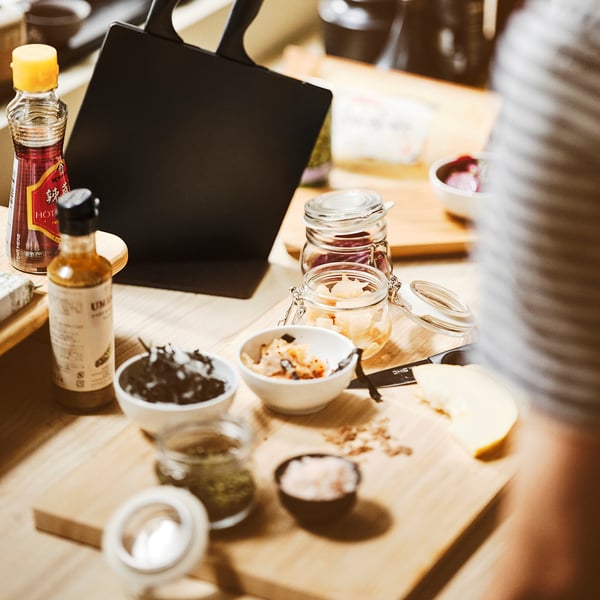 Tavolo in legno con sottaceti, condimenti e un computer portatile. I barattoli KORKEN sono utilizzati per la conservazione ermetica.