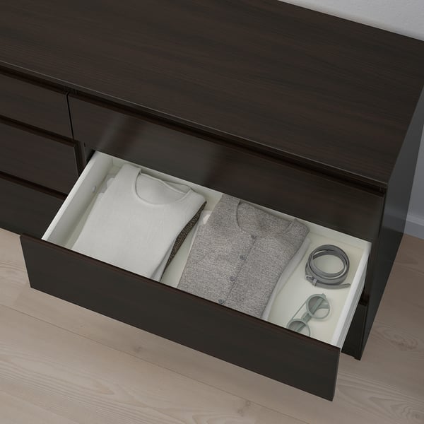 Cassettiera scura aperta con vestiti e accessori ben piegati nel cassetto bianco.