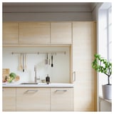 Cucina moderna con armadi in legno chiaro, ripiani bianchi e un binario in metallo che contiene gli utensili da cucina.