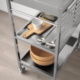 Moderno carrello da cucina in acciaio inox con ruote, dotato di utensili, tagliere e ciotole, perfetto per la preparazione dei cibi in piccoli spazi.