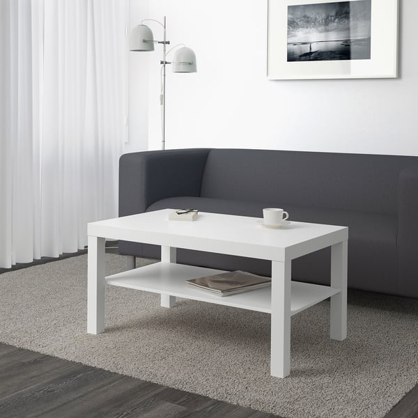 Soggiorno moderno con elegante tavolino bianco LACK di fronte al divano grigio, con in mano una tazza e una pila di libri.