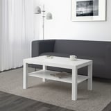 Soggiorno moderno con elegante tavolino bianco LACK di fronte al divano grigio, con in mano una tazza e una pila di libri.