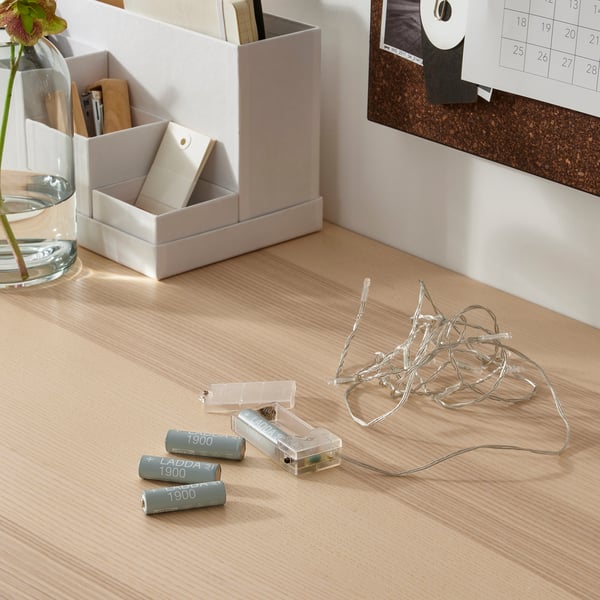 Scrivania in legno con forniture per ufficio: batterie LADDA, caricabatterie, catenarie, organizer da scrivania, vaso con fiori, bacheca e calendario.