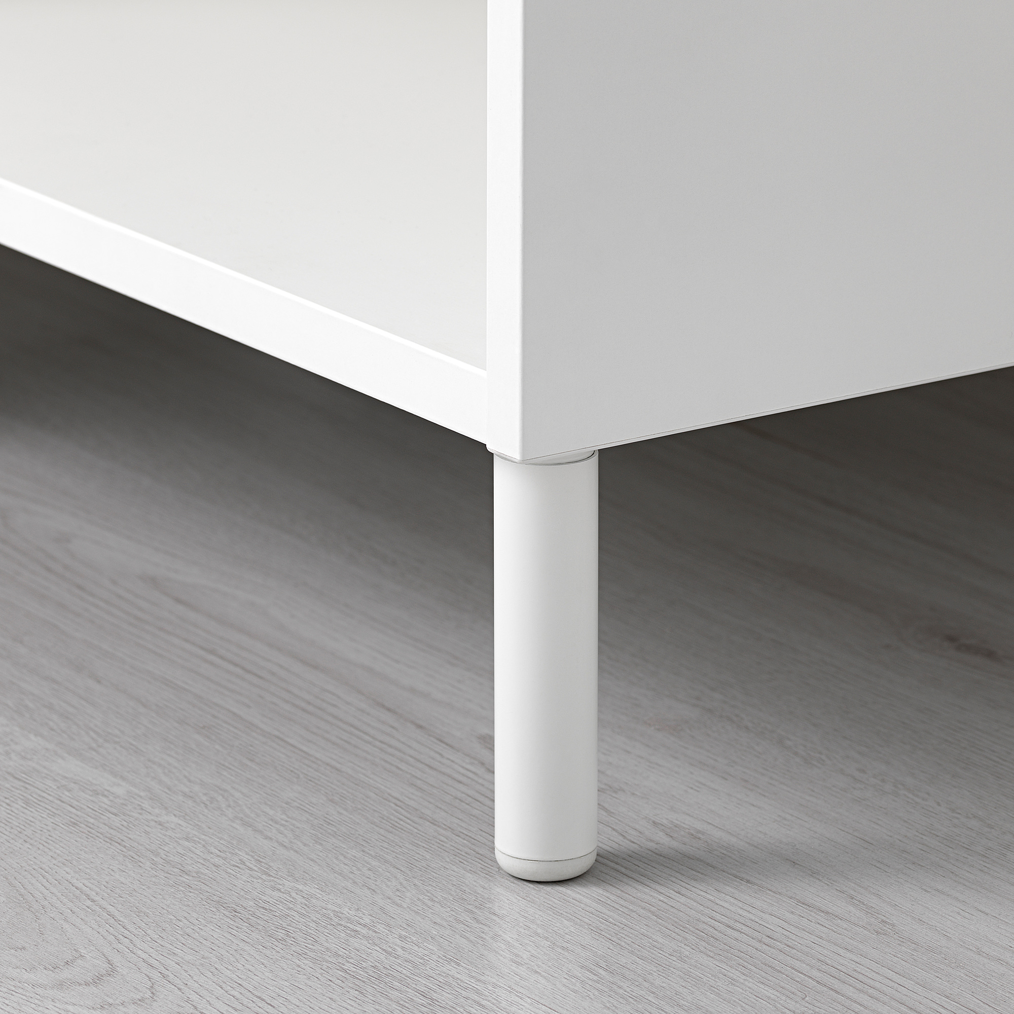 Gamba in metallo bianco con piedino regolabile su pavimento in legno.
