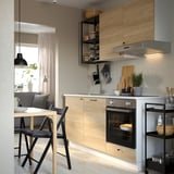 Cucina moderna con armadi in legno chiaro, forno in acciaio inox e sedie nere.