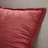 Cuscino rosso primo piano, bordo strutturato su grigio.