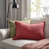 Soggiorno con divano grigio, cuscino rosa-rosso, cuscino verde, lampada nera e fiori bianchi.