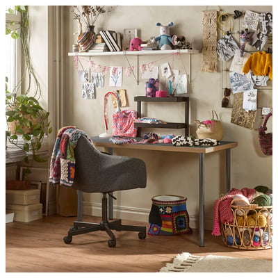 Stanza del bricolage con scrivania LAGKAPTEN, scaffali con filati, articoli a maglia e oggetti decorativi. Sedie grigie, piante e decorazioni murali.
