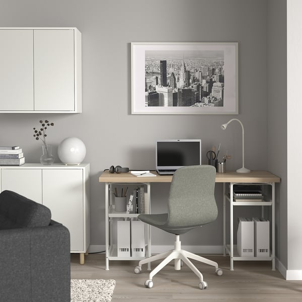 Home office moderno e minimalista con scrivania LAGKAPTEN, arte del paesaggio urbano, sedia grigia e accessori eleganti.