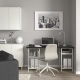 Scrivania angolare moderna con piano nero, gambe bianche, ripiani aperti, sedia neutra, arte del paesaggio urbano.