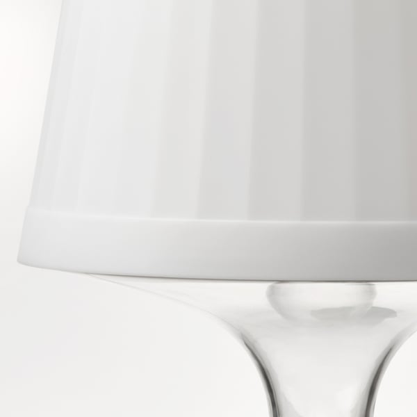 L'immagine mostra una lampada elegante e moderna con un paralume bianco e una base in policarbonato trasparente. Ben progettato, portatile e versatile.