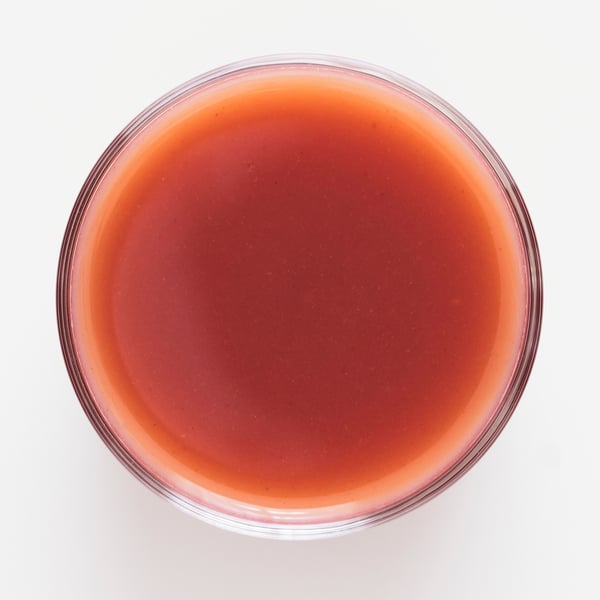 Una ciotola di vetro trasparente riempita con un frullato denso di frutti rossi dalla consistenza lucida. Fragole fresche, lamponi e mirtilli in evidenza.