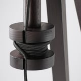 Lampada da palo in legno scuro con altezza regolabile, dotata di portacavi a spirale all'interno della sua base, progettata per un uso organizzato e flessibile.