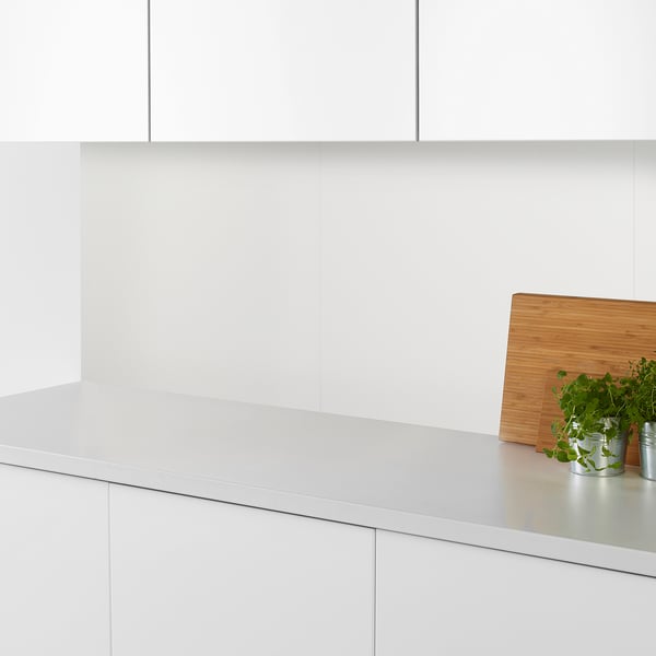 Cucina moderna con piano di lavoro bianco, tagliere in legno e piccole piante in vaso in contenitori di metallo.