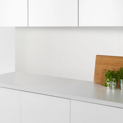 Cucina moderna con piano di lavoro bianco, tagliere in legno e piccole piante in vaso in contenitori di metallo.
