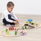 Un bambino gioca con un trenino in legno, che comprende binari, blocchi e una locomotiva a batteria con funzioni di avanti, indietro e arresto.