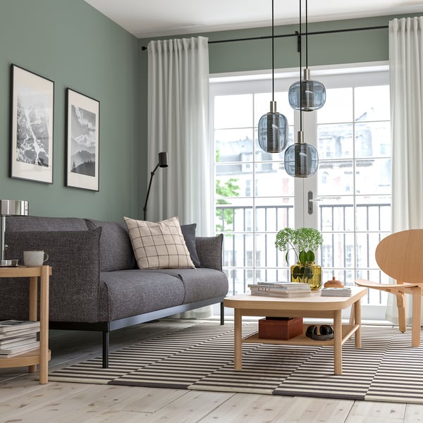 Soggiorno moderno con tavolino grigio LISTERBY, rovere, tappeto a righe, grande finestra e divano grigio.