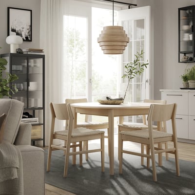 Moderna sala da pranzo con tavolo rotondo in legno, quattro sedie, elegante lampada, tappeto grigio e porta aperta, con tappeto LUFTFARTYG in toni neutri.