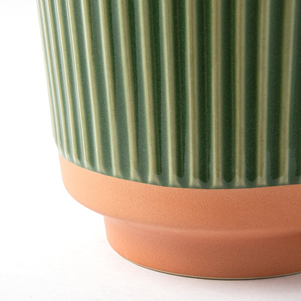 Primo piano di un vaso céramique verde strutturato con base in terracotta, che mostra il suo design tattile e rigato e la finitura liscia.