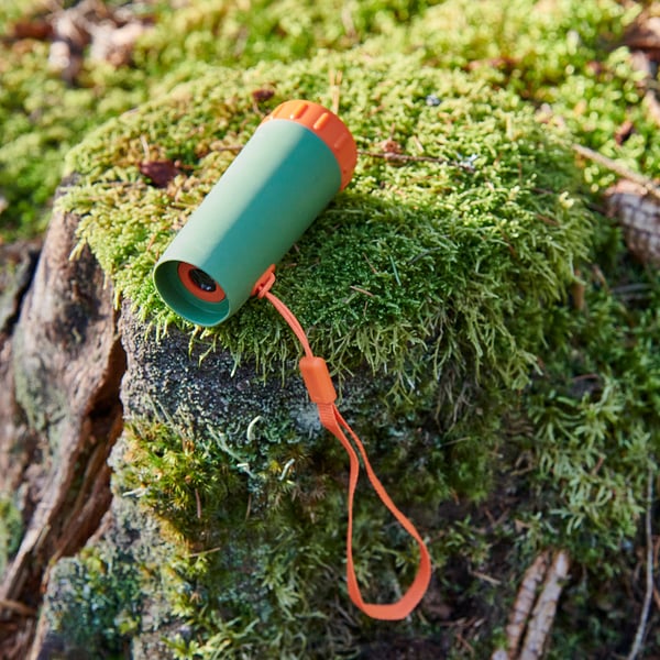 Tronco muschioso con telescopio verde, cinturino arancione. Giocattolo per l'esplorazione della natura. Durevole, colorato.