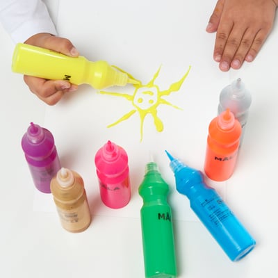 I bambini spremono bottiglie di vernice colorate MÅLA sulla carta; Le mani tengono la bottiglia gialla mentre altre mostrano vari colori.