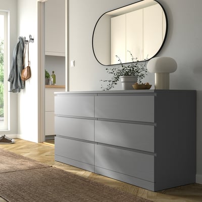 Camera da letto moderna con grande comò MALM grigio, specchio rotondo, lampada e piante. Legno tinto grigio, cassetti lisci, ancorati a parete.