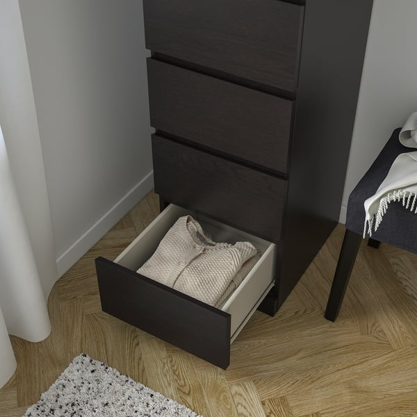 Comò moderno con un cassetto aperto che rivela i vestiti ben piegati. Finitura scura, tre cassetti totali, sicuro per i bambini quando ancorato.