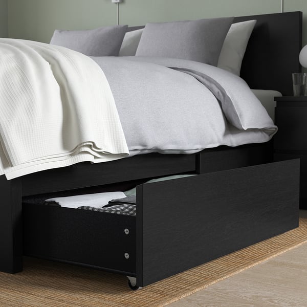 Giroletto in legno nero con cassetti. Ha una testiera alta e integra scatole portaoggetti su ruote per un facile accesso alla biancheria da letto extra.